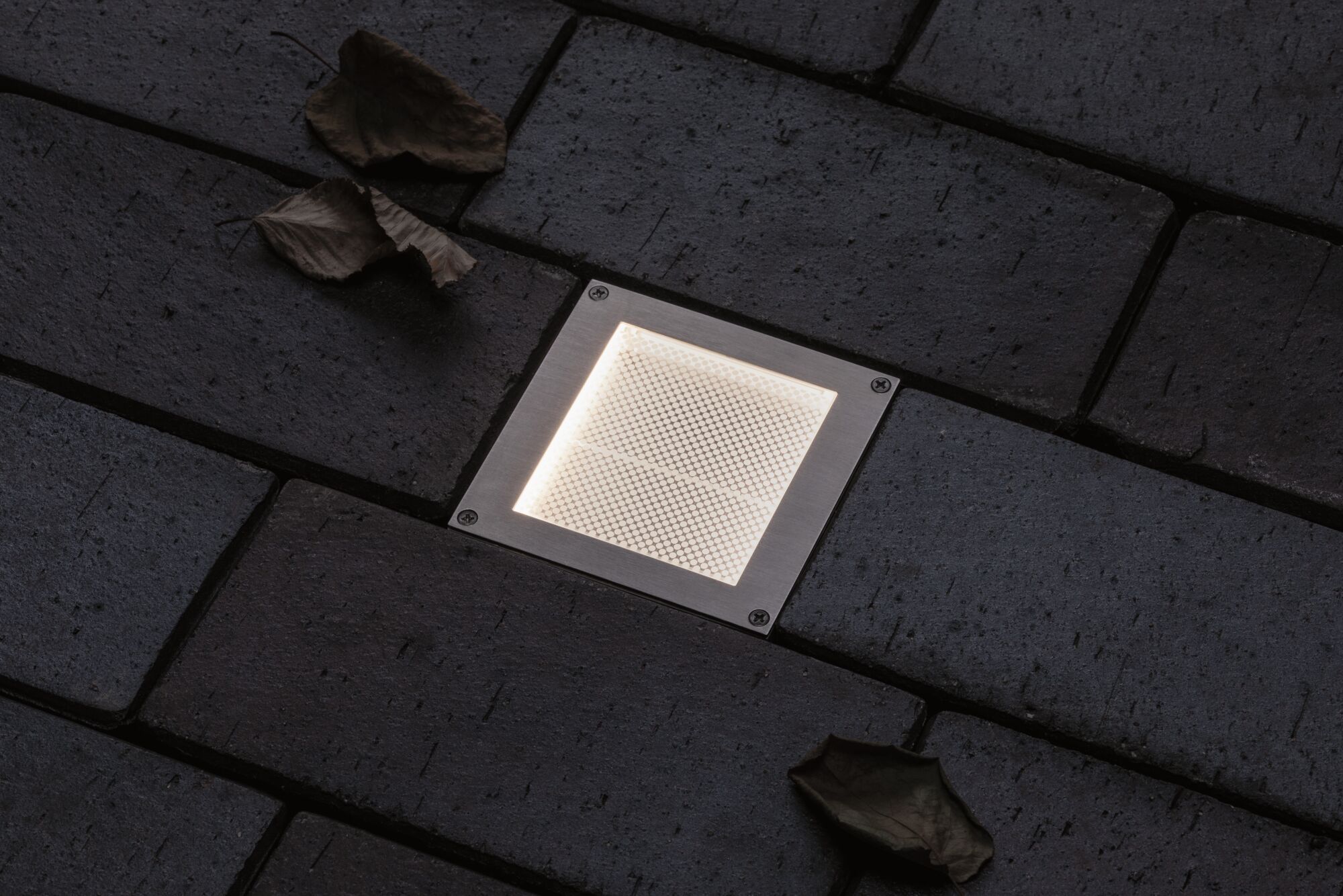 Eingelassene quadratische LED-Bodenleuchte aus Edelstahl mit warmweißem Licht auf dunklem Pflaster