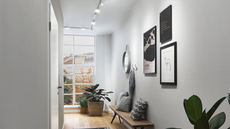 Modern hallway with white aluminum LED ceiling lights, wooden bench, and indoor plants.