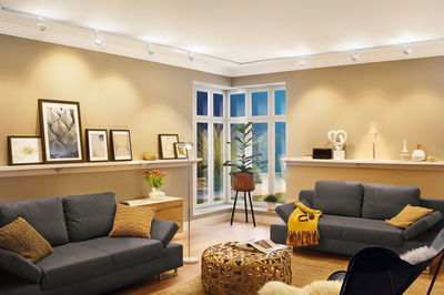 Moderne woonkamer met grijze banken, houten vloerkleed en witte URail railsysteem plafondverlichting