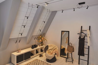 Black cable track lighting with multiple spotlights on slanted ceiling in modern dressing room with chair and mirror
