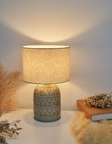 Keramik-Tischlampe mit cremefarbenem Stoffschirm und floralem Muster, warmes Wohnlicht.