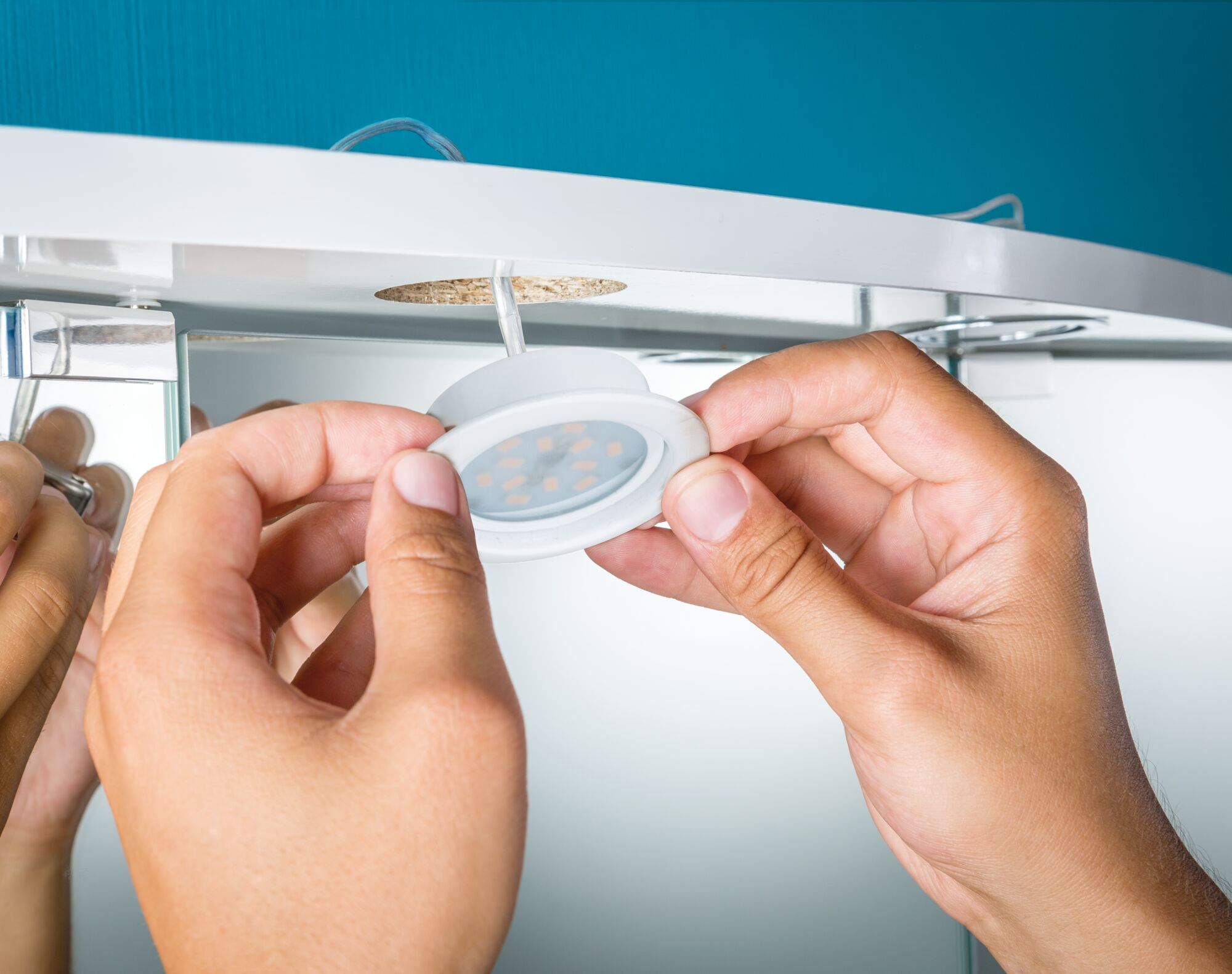 Hands installing white LED recessed light under white furniture with cable connection