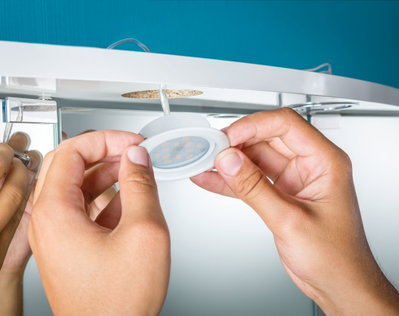 Hands installing white LED recessed light under white furniture with cable connection