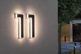 Modern black LED house number light with warm white illumination mounted on exterior wall for entrance