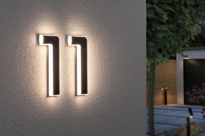 Moderne sort LED-husnummerlampe med varmt hvidt lys monteret på ydervæg ved indgang