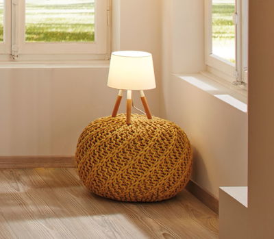 Moderne tafellamp met witte kap en houten poten op gele gebreide poef in woonkamer.