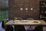 Salle à manger moderne avec table en bois clair, chaises noires et trois suspensions blanches sur mur en briques.