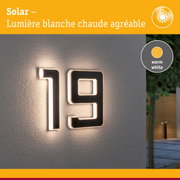 Numéro de maison solaire en matériau noir avec lumière LED blanc chaud sur mur gris