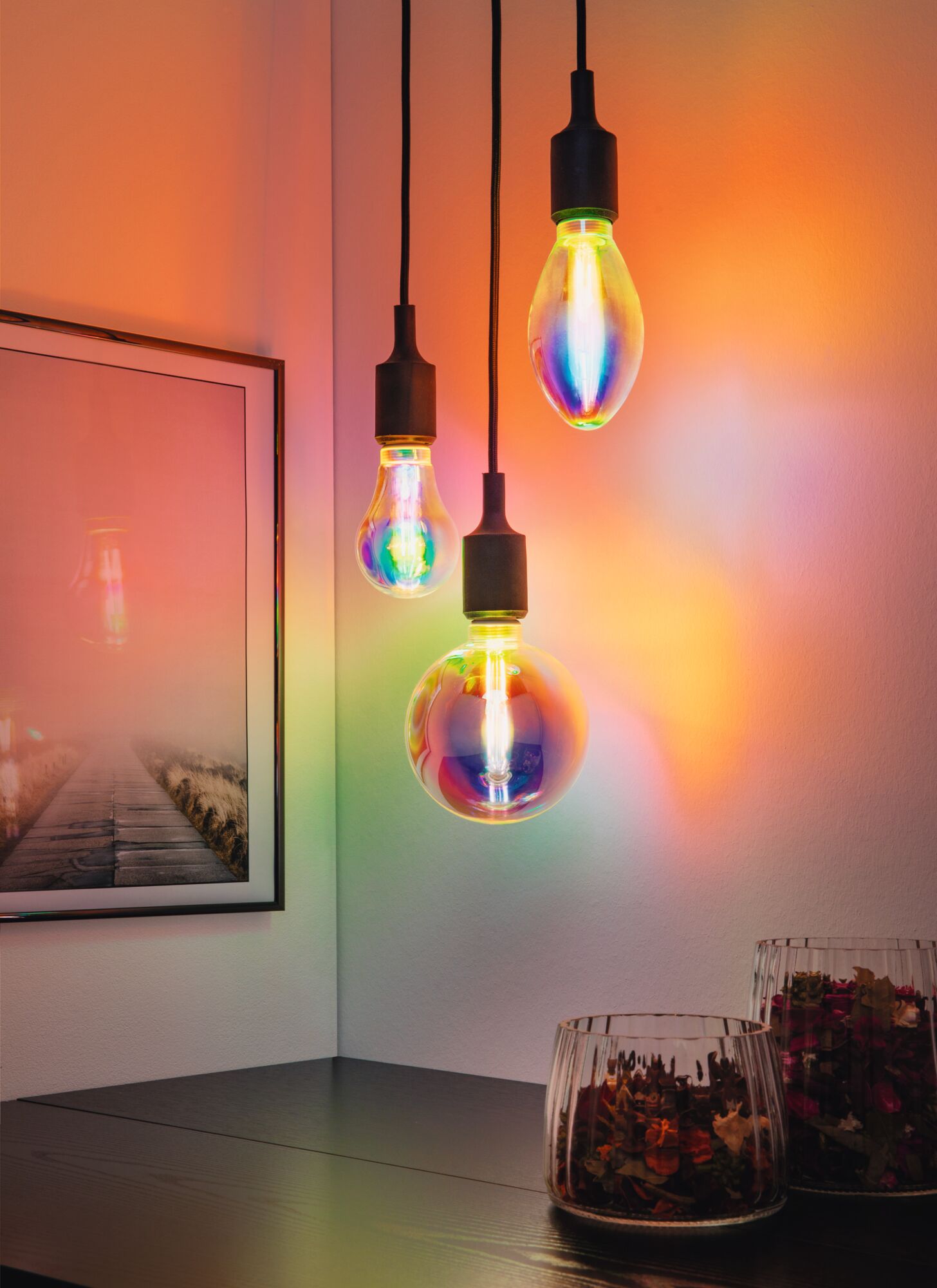 Kleurrijke LED-hanglampen met zwarte snoeren aan witte muur, moderne inrichting met levendige lichteffecten.