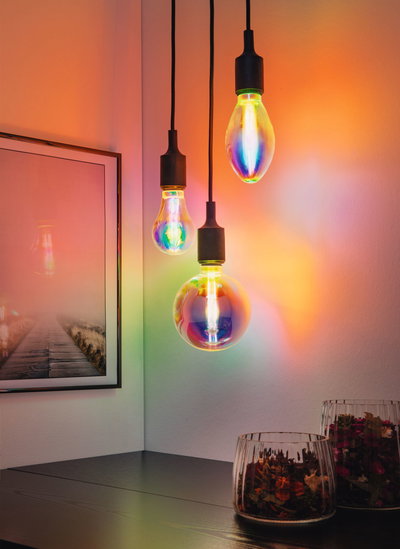 Kleurrijke LED-hanglampen met zwarte snoeren aan witte muur, moderne inrichting met levendige lichteffecten.