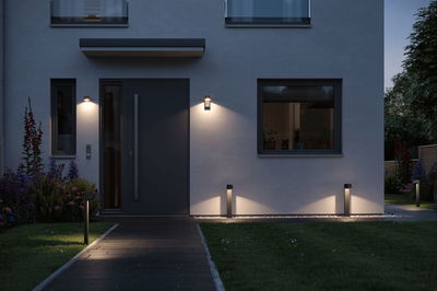 Moderne buitenverlichting met zwarte LED-wandlampen en paaltjes langs huisgevel en tuinpad