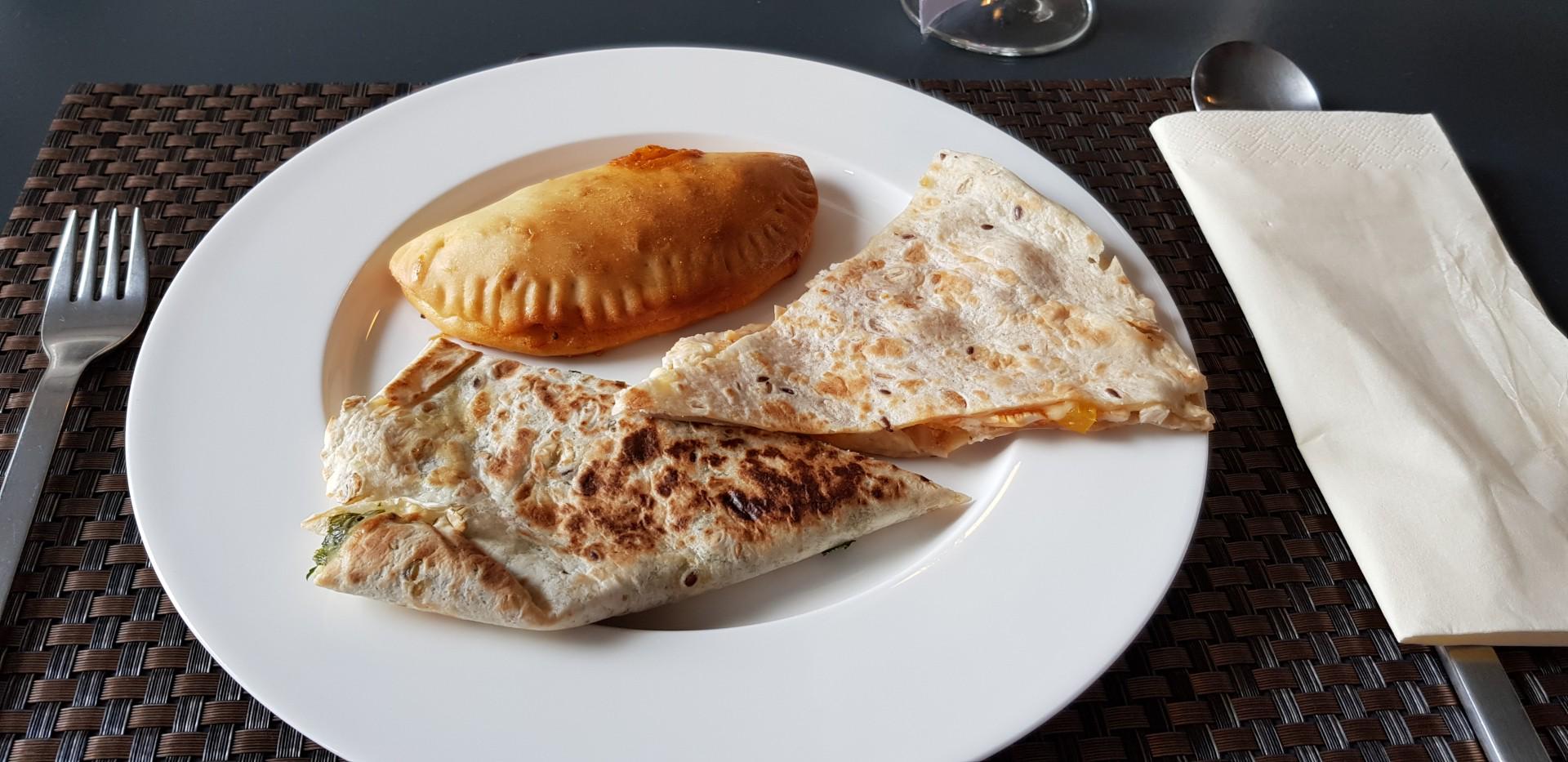 Weißer Teller mit gefülltem Teigtaschen und zwei gefalteten Fladenbroten auf dunklem Tisch mit Besteck.