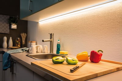 Moderne Küchenarbeitsplatte mit Edelstahlspüle, LED-Unterbauleuchte und bunten Paprikaschoten auf Holzbrett