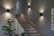 Moderne schwarze Metall-Wandleuchte mit dekorativem Lichtmuster an Treppenhauswand für Wohnraumbeleuchtung