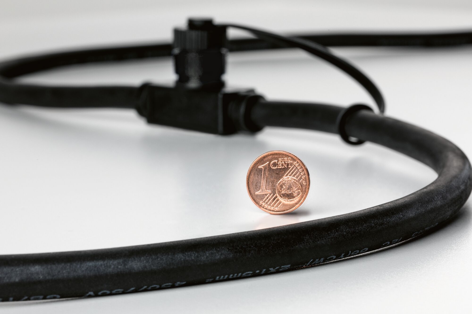 Schwarzes Kabel mit blauem Verbinder neben 1-Cent-Münze zur Größenveranschaulichung für LED-Beleuchtung.