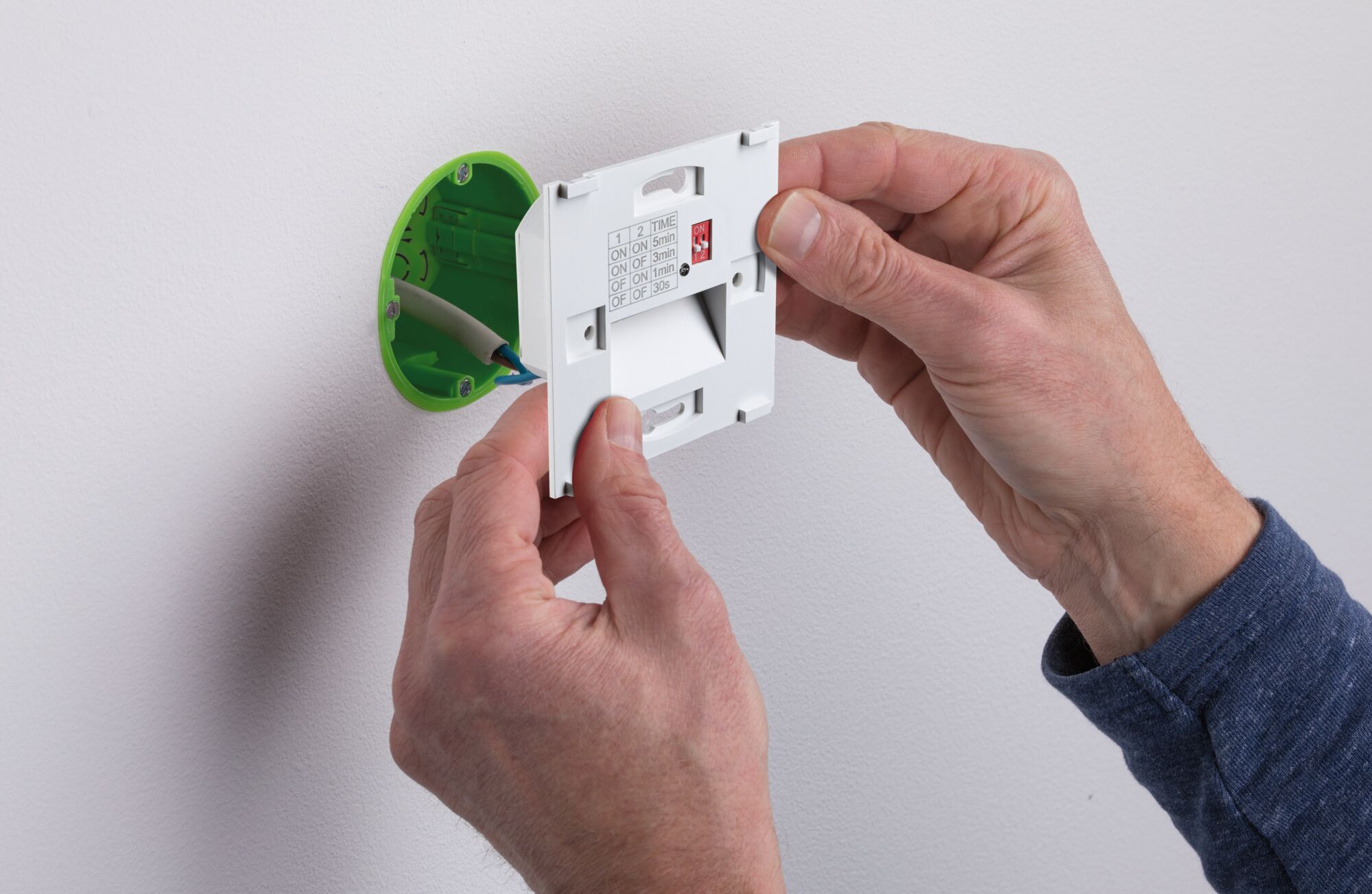 Hände montieren weißen Zeitschalter mit grüner Unterputzdose an weiße Wand für Lichtsteuerung