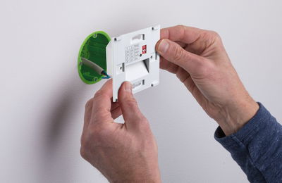 Hände montieren weißen Zeitschalter mit grüner Unterputzdose an weiße Wand für Lichtsteuerung