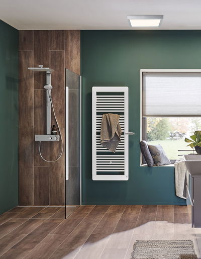 Salle de bain moderne avec radiateur porte-serviettes blanc sur mur vert et sol en carrelage bois