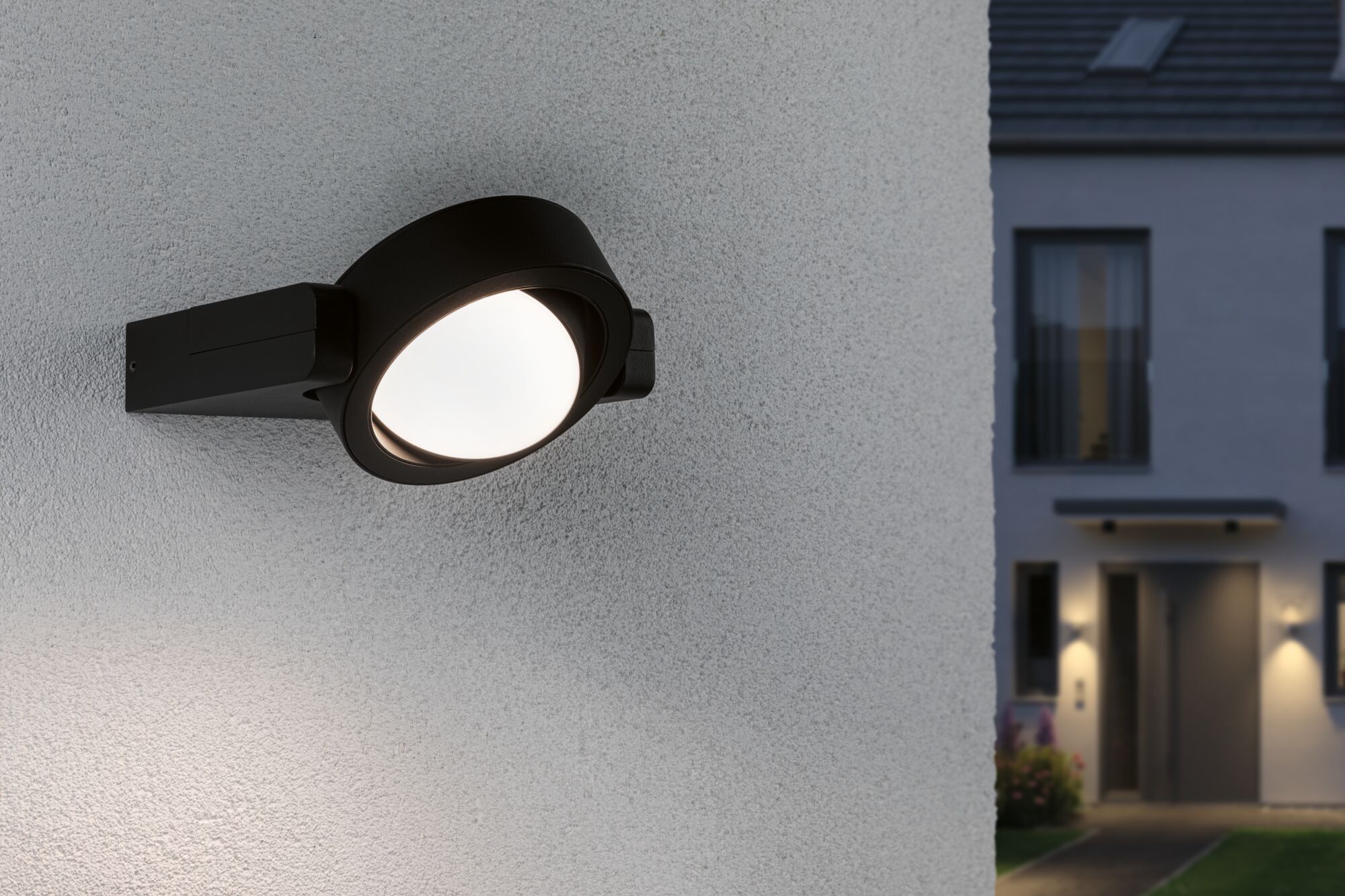 Schwarze Außenwandleuchte aus Metall mit rundem, weißem Leuchtmittel an Hauswand bei Dämmerung