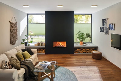 Gemütliches Wohnzimmer mit weißem Sofa, Holzboden, schwarzem Kamin und moderner Deckenbeleuchtung.