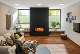 Gemütliches Wohnzimmer mit weißem Sofa, Holzboden, schwarzem Kamin und moderner Deckenbeleuchtung.