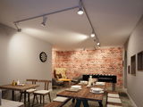 Moderner Raum mit weißen Paulmann LED-Strahlern an Schienensystem, roter Backsteinwand und Holzmöbeln.