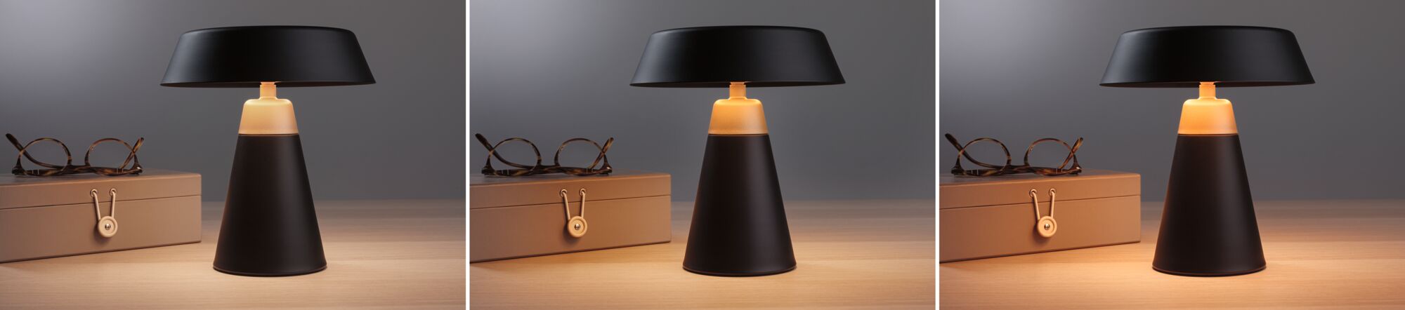 Schwarze Tischlampe aus Metall mit warmweißem Licht neben brauner Brillenbox auf Holztisch