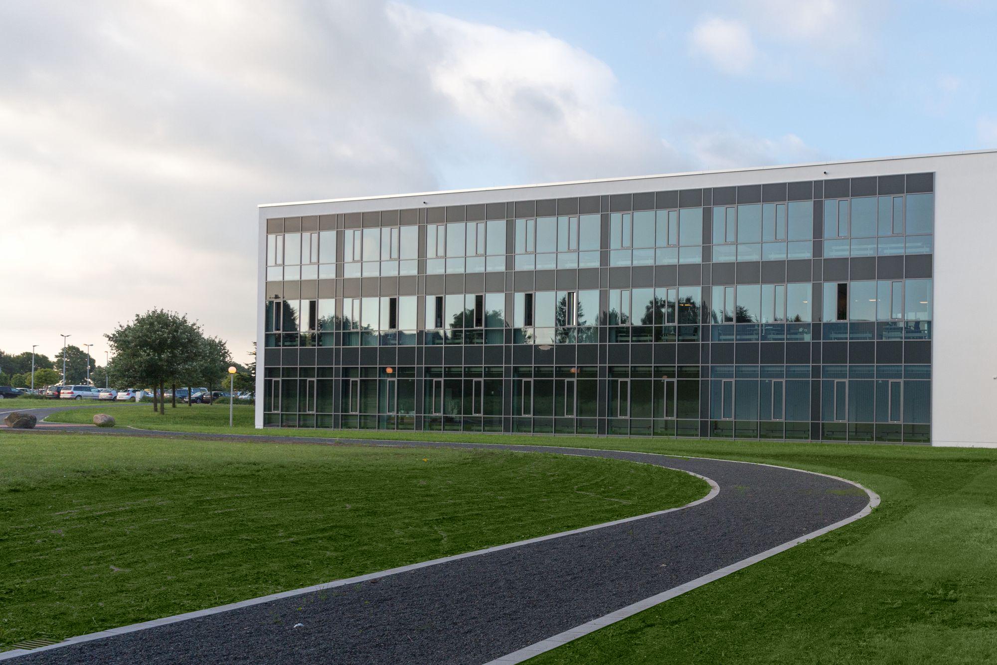 Modern office building with large glass windows and green lawn in front under cloudy sky