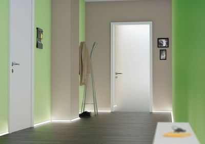 Modern hallway with white doors, green walls, and LED floor lighting for stylish interior design