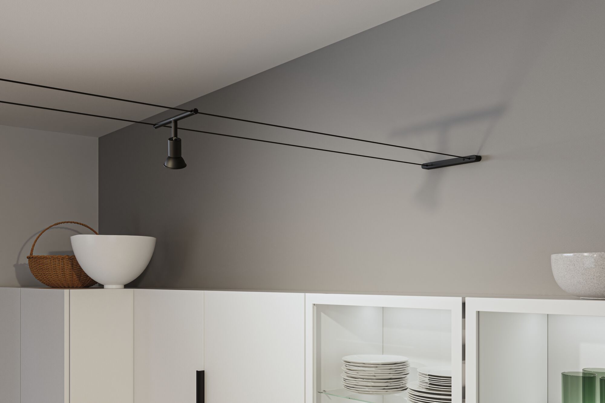 Black cable spotlight on grey wall above white kitchen cabinet with dishes and decor
