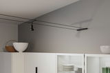 Black cable spotlight on grey wall above white kitchen cabinet with dishes and decor