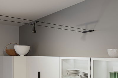 Black cable spotlight on grey wall above white kitchen cabinet with dishes and decor
