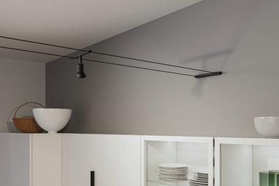 Spot noir sur câble sur mur gris au-dessus d'un meuble de cuisine blanc avec vaisselle et décoration