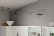 Schwarze Seilstrahlerleuchte an grauer Wand über weißem Küchenschrank mit Geschirr und Dekoration