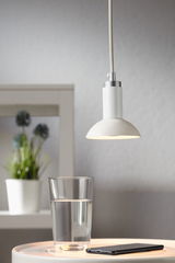 White metal pendant lamp with fabric cable above glass of water and smartphone on table, modern LED lighting