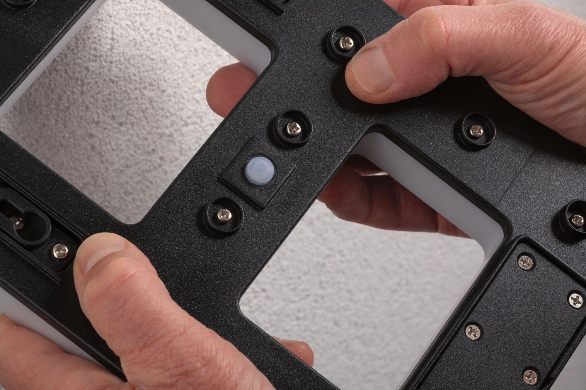 Black plastic housing with screws and on/off switch held by hands, close-up view.