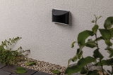 Black metal LED wall light on white exterior wall with gravel and garden plants