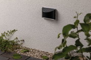 Black metal LED wall light on white exterior wall with gravel and garden plants