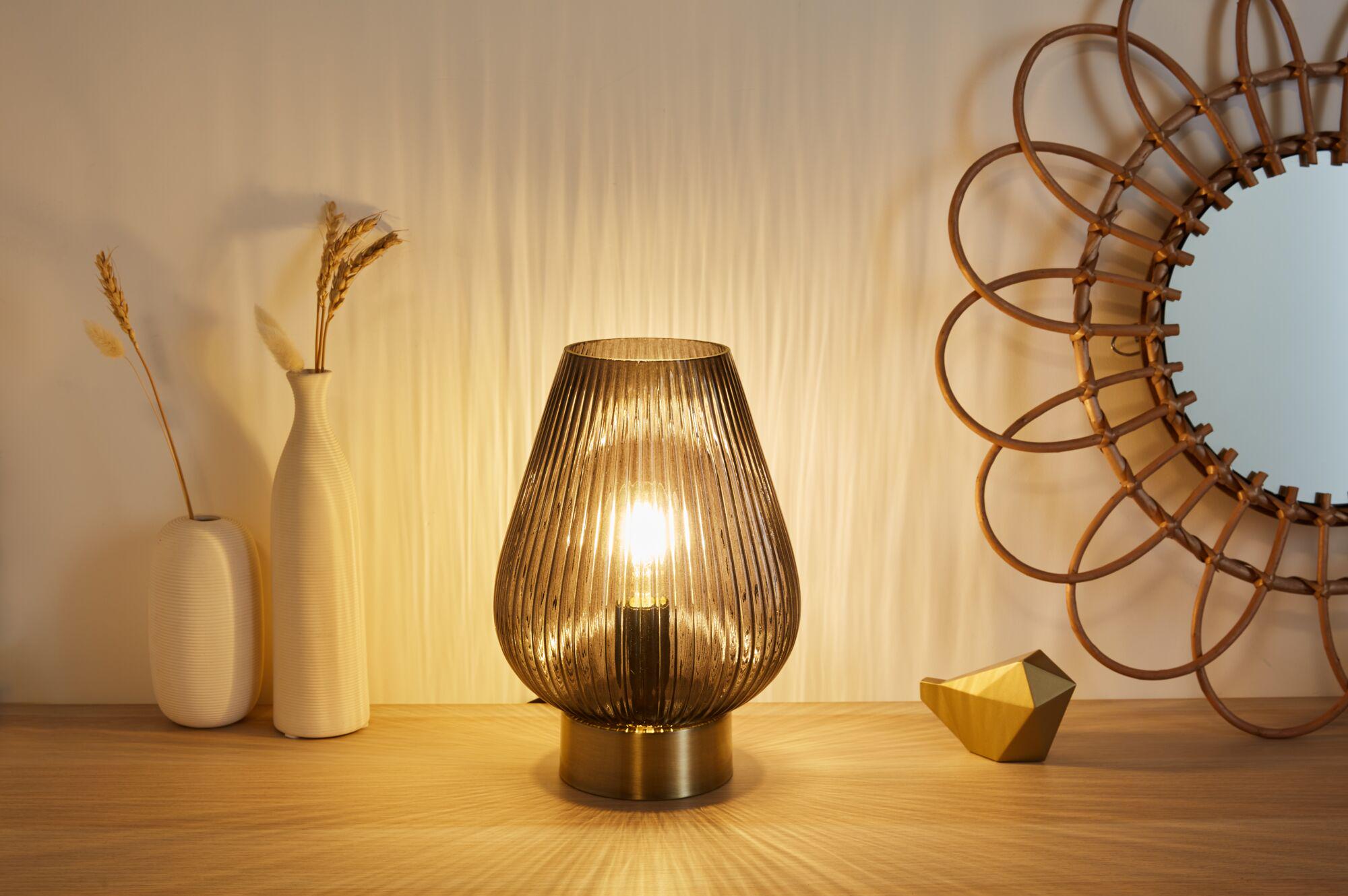 Modern brown ribbed glass table lamp with brass base on wooden surface next to decor and mirror