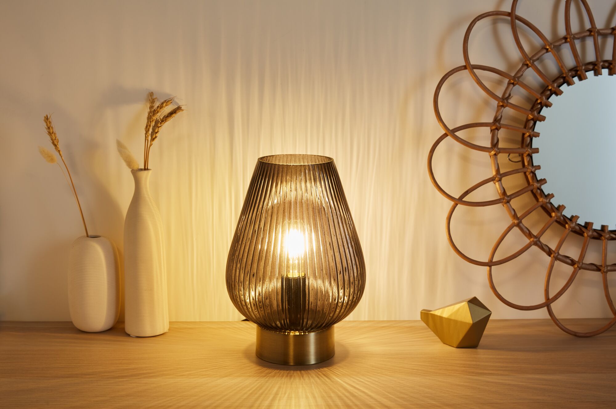 Modern brown ribbed glass table lamp with brass base on wooden surface next to decor and mirror