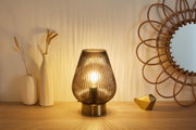Modern brown ribbed glass table lamp with brass base on wooden surface next to decor and mirror