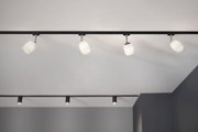 Vier weiße Glas-Spotlights an schwarzer Schiene für moderne Innenbeleuchtung im Raum