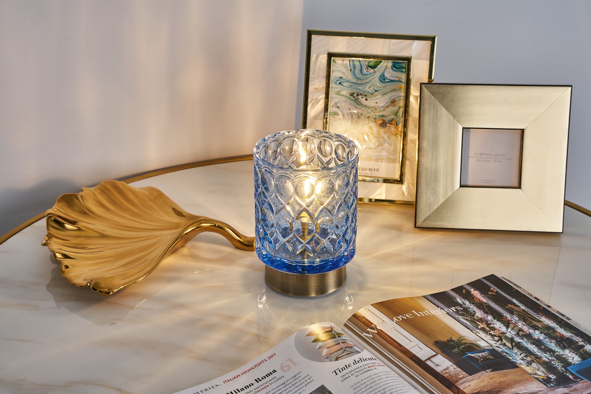 Blauw glaslicht met patroon en messing voet op marmeren tafel met gouden decoratie en fotolijsten