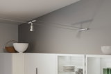 Moderner weißer Seilstrahler aus Metall an grauer Wand über weißem Küchenschrank mit Geschirr.