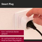 Weißer Smart Plug aus Kunststoff mit Knopf, an Wandsteckdose mit schwarzem Kabel angeschlossen