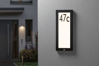 Schwarze LED-Hausnummernleuchte mit weißer Leuchtfläche und Zahl 47c an grauer Wand außen