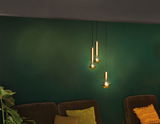 Three gold pendant lights with bulbs hanging against green wall above brown sofas with cushions.