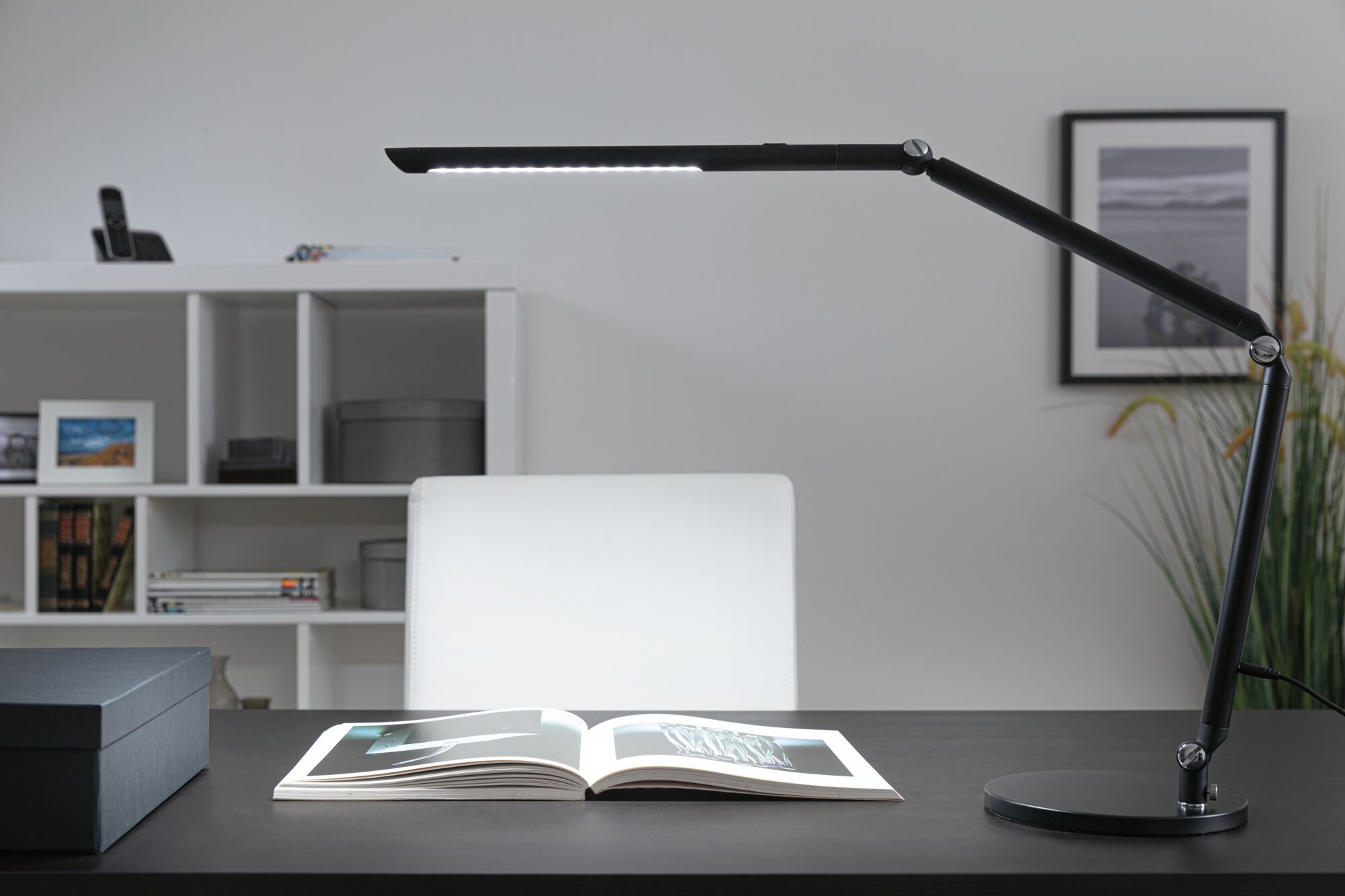 Schwarze LED-Schreibtischlampe mit verstellbarem Arm auf dunklem Tisch mit offenem Buch, moderne Bürobeleuchtung