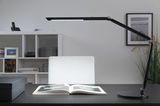 Schwarze LED-Schreibtischlampe mit verstellbarem Arm auf dunklem Tisch mit offenem Buch, moderne Bürobeleuchtung