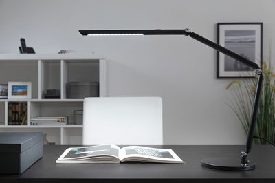 Schwarze LED-Schreibtischlampe mit verstellbarem Arm auf dunklem Tisch mit offenem Buch, moderne Bürobeleuchtung